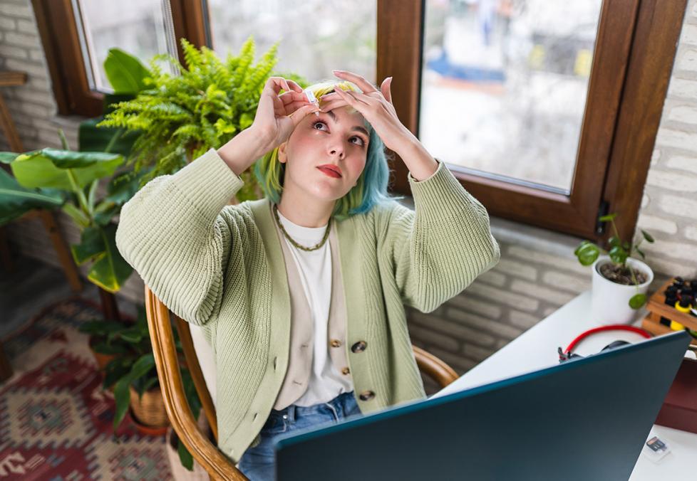 A young woman using eye drops in her home