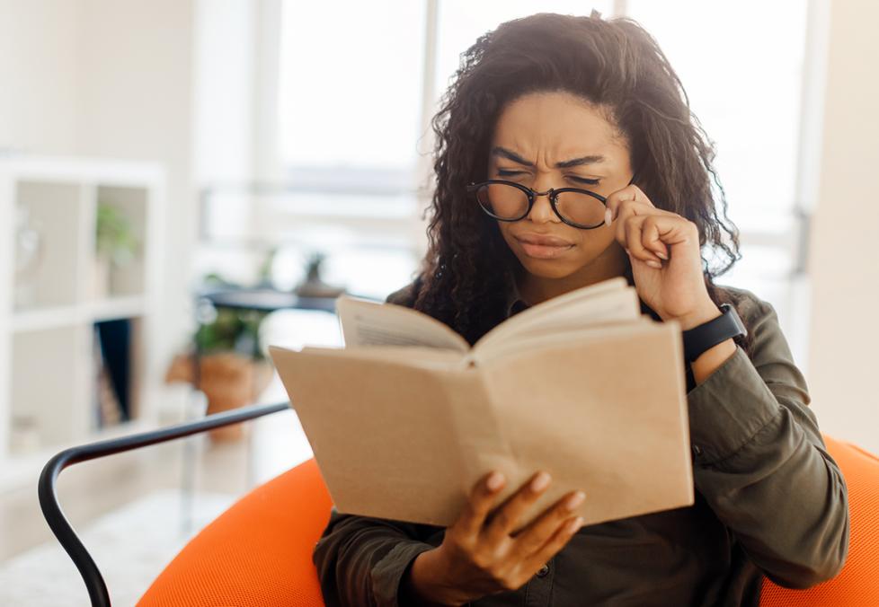 A young woman putting on glasses to read a book