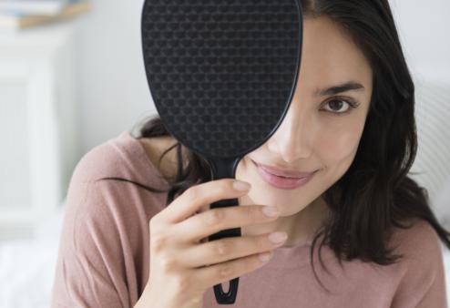 Woman covering one eye with a hand mirror.