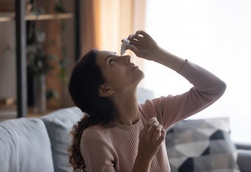 A young woman using eye drops in her home